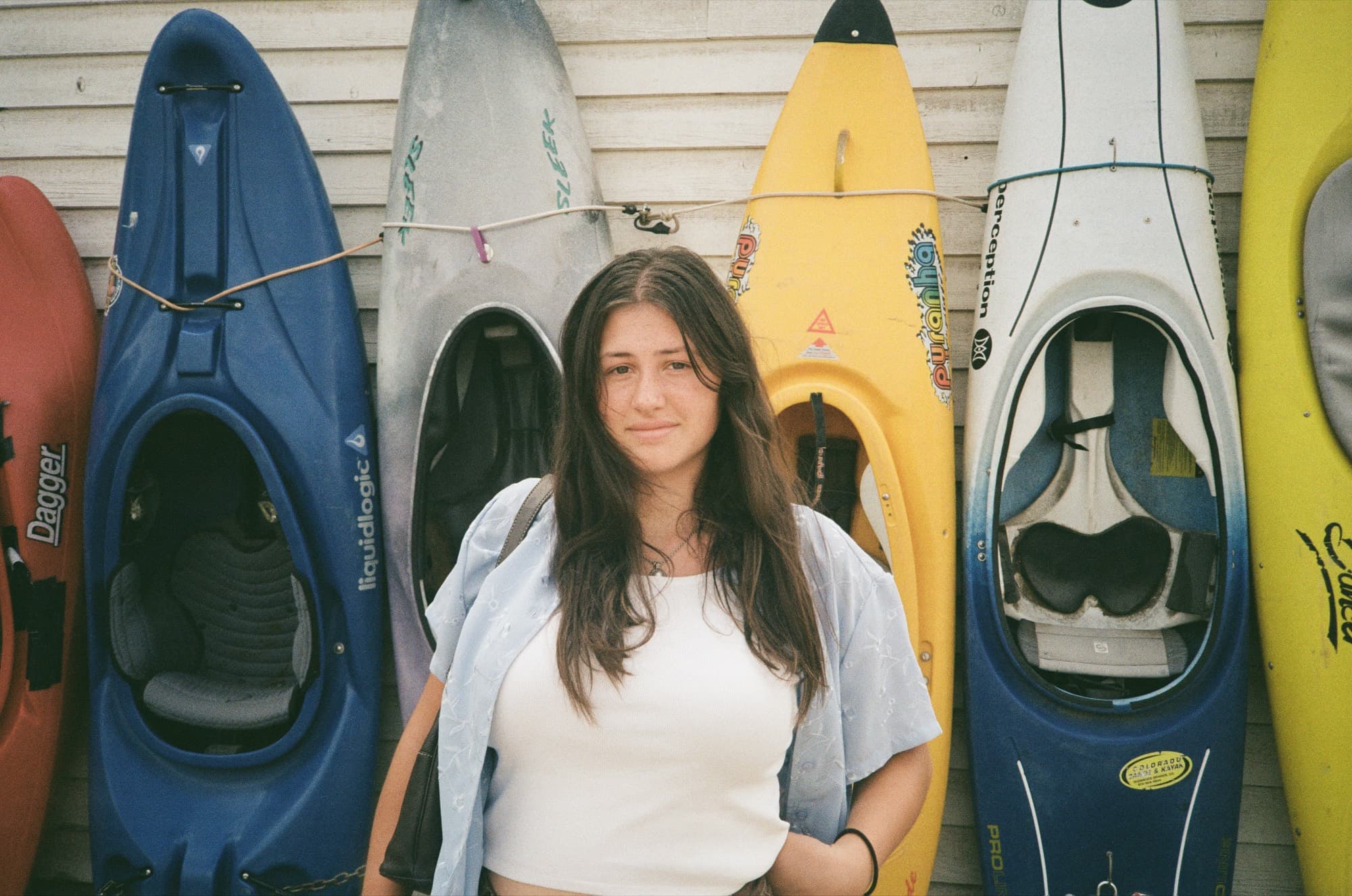 A woman standing in front of a row of kayaks propped against a clapboard wall