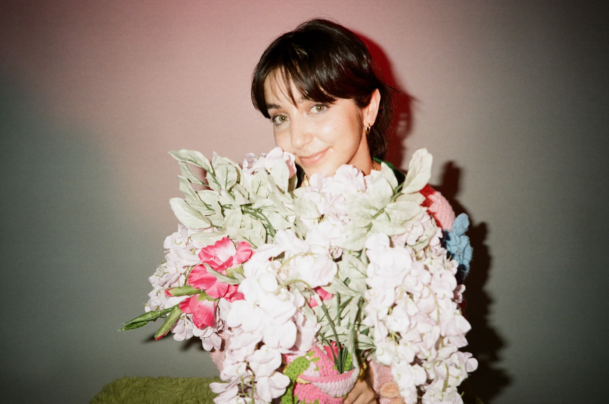 A woman holding a large bouquet of pale stock flowers in a pink-lit room