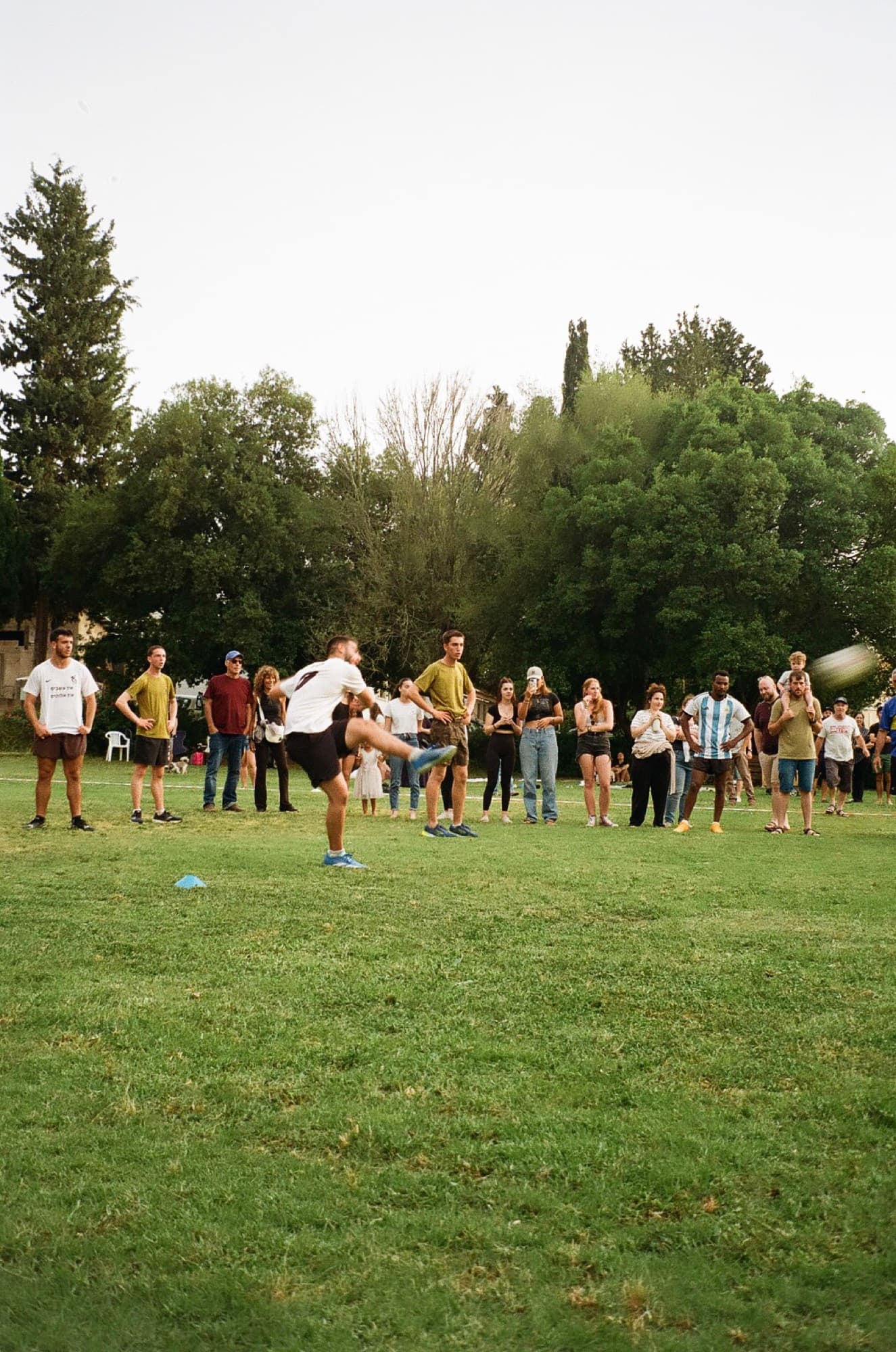 A footballer striking the ball on a grass pitch while a crowd watches from the touchline
