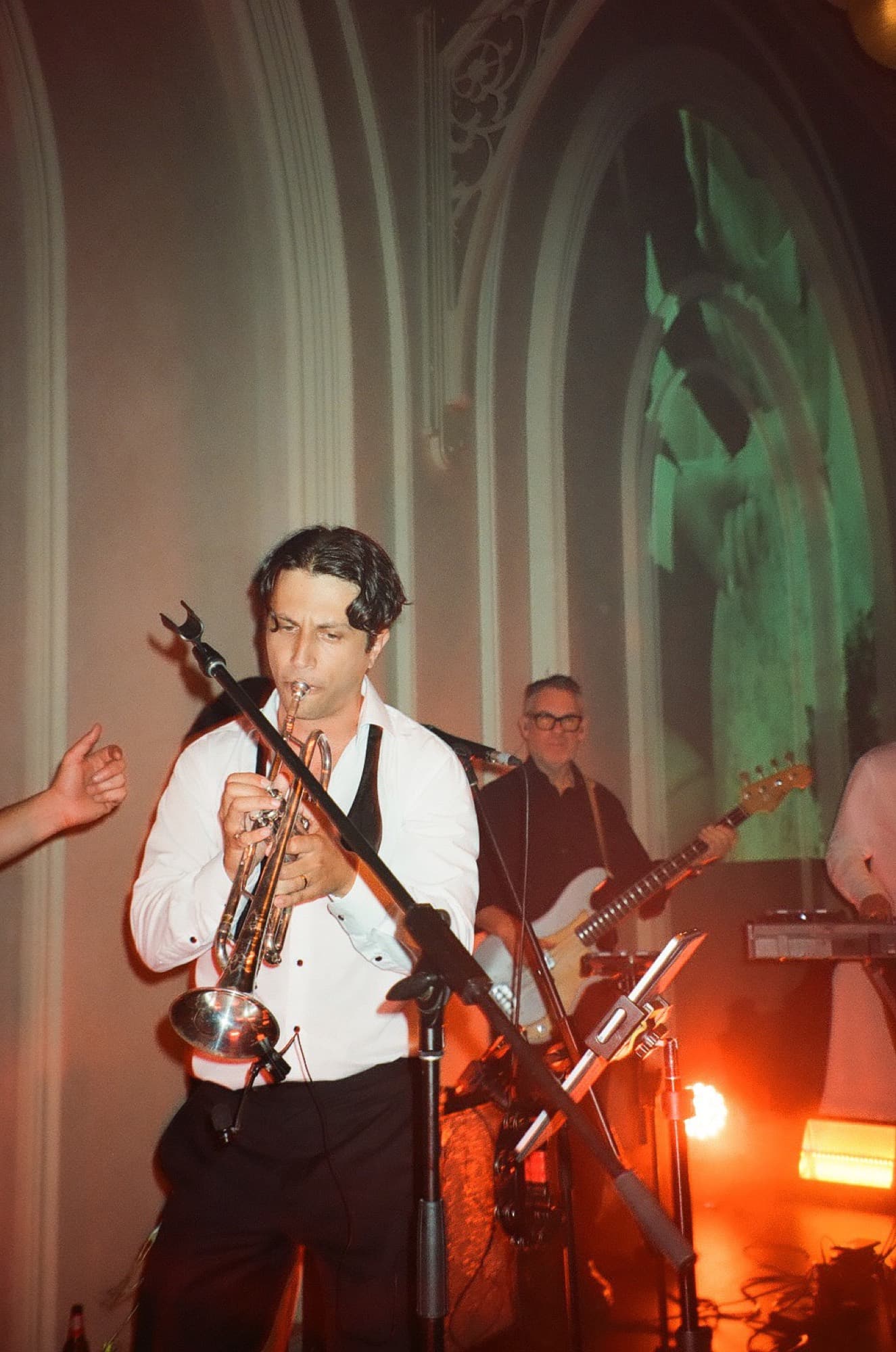 A trumpeter playing with a band beneath tall arched windows